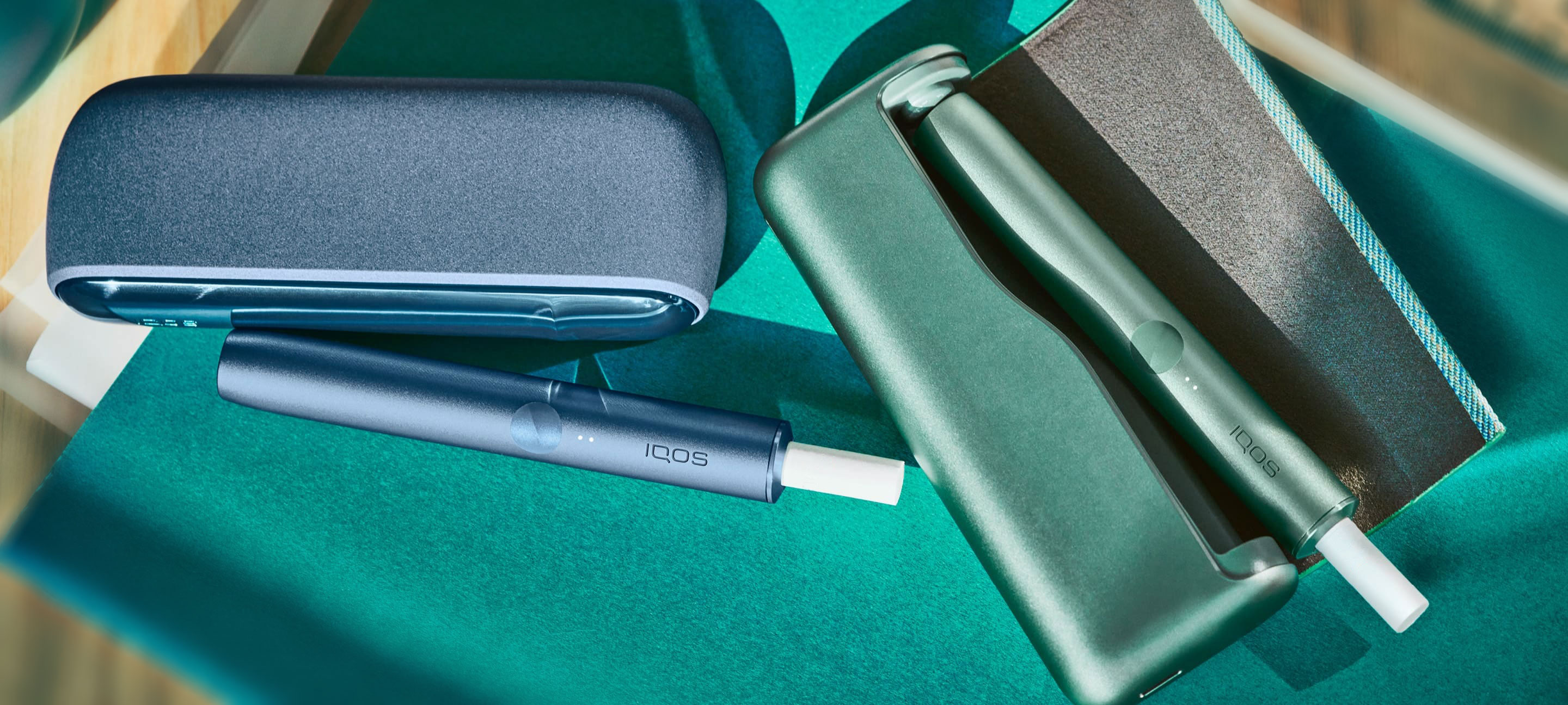 An Azure Blue IQOS ILUMA Holder and Pocket Charger and a Jade Green Holder in a full wrap.