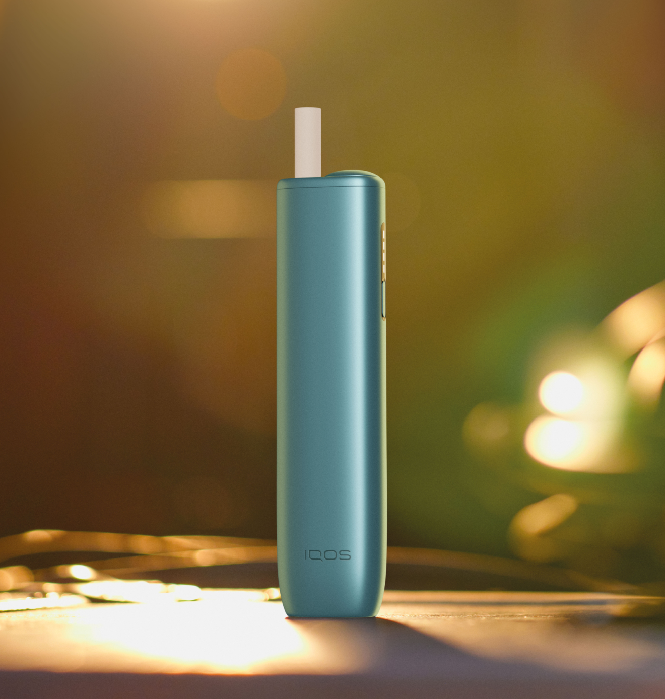 A jade green IQOS device on a table next to an IQOS product box.