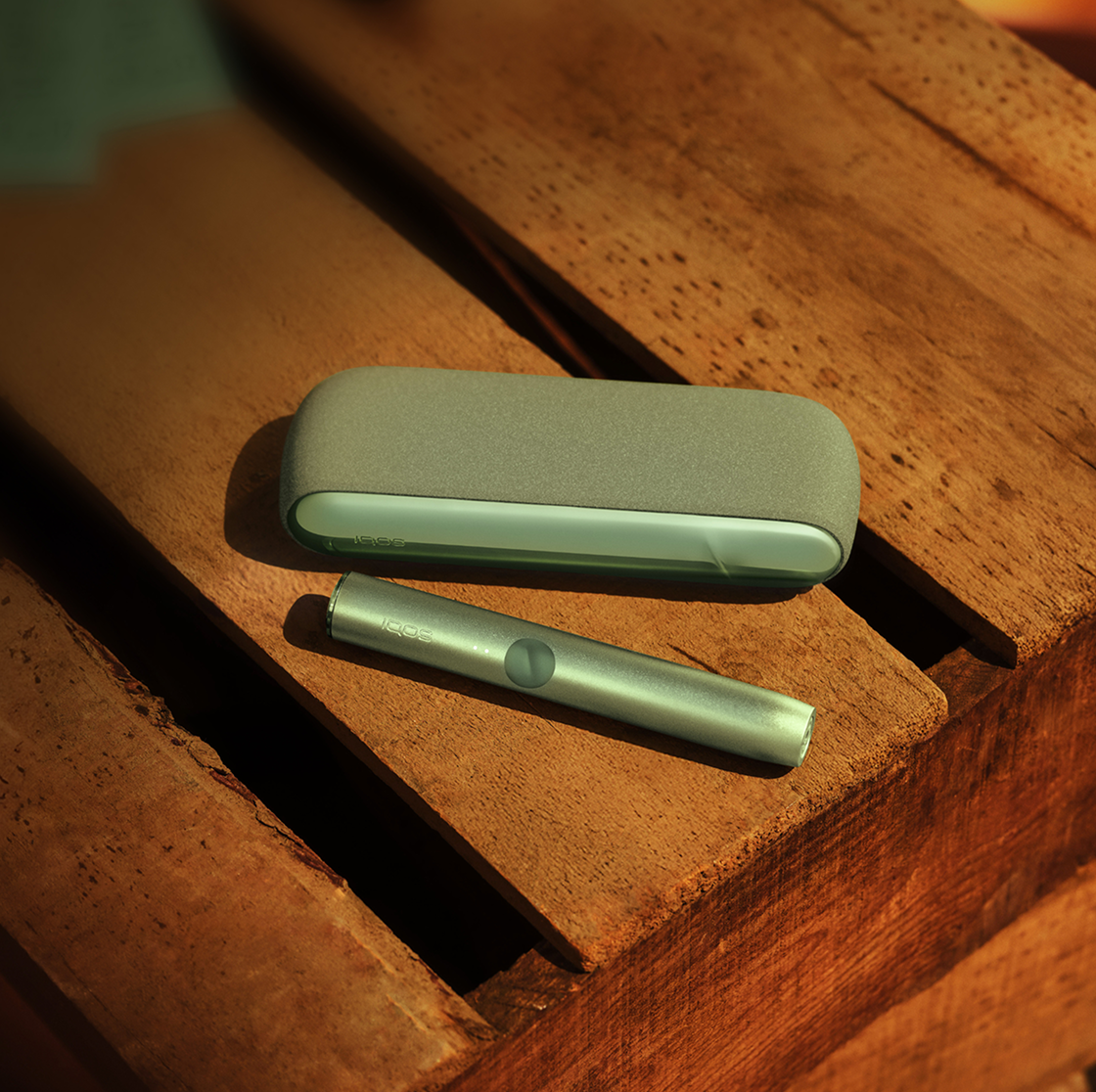 An IQOS ILUMA device on a rock next to an outdoor bag.