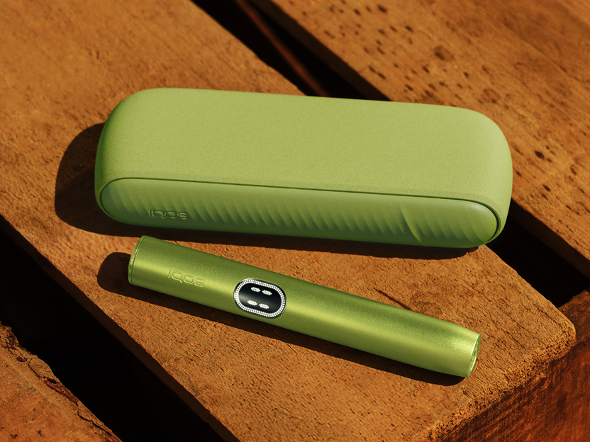 A Leaf Green IQOS ILUMA i device on a wooden table.