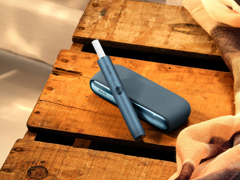 A Sunset Red IQOS ILUMA device on top of a table.