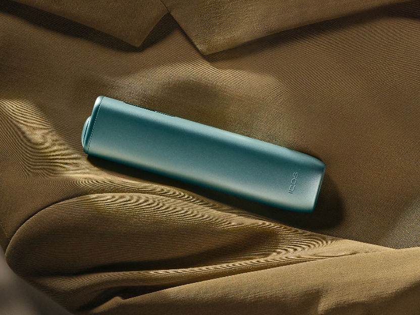 Un appareil IQOS  ILUMA i ONE Noir Minuit posé sur un manteau.