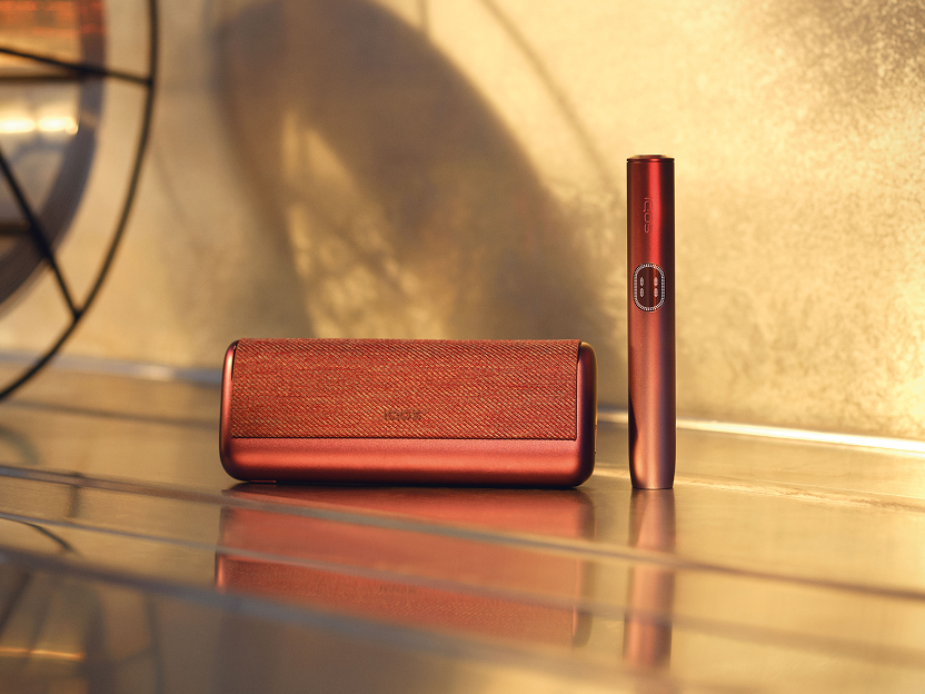 A Garnet Red IQOS ILUMA i PRIME device on the floor.