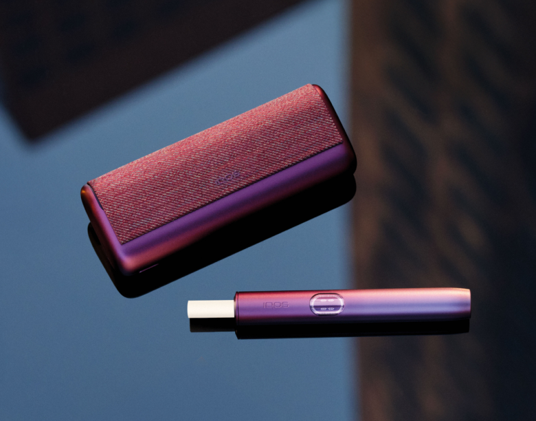 An IQOS ILUMA device on a rock next to an outdoor bag.