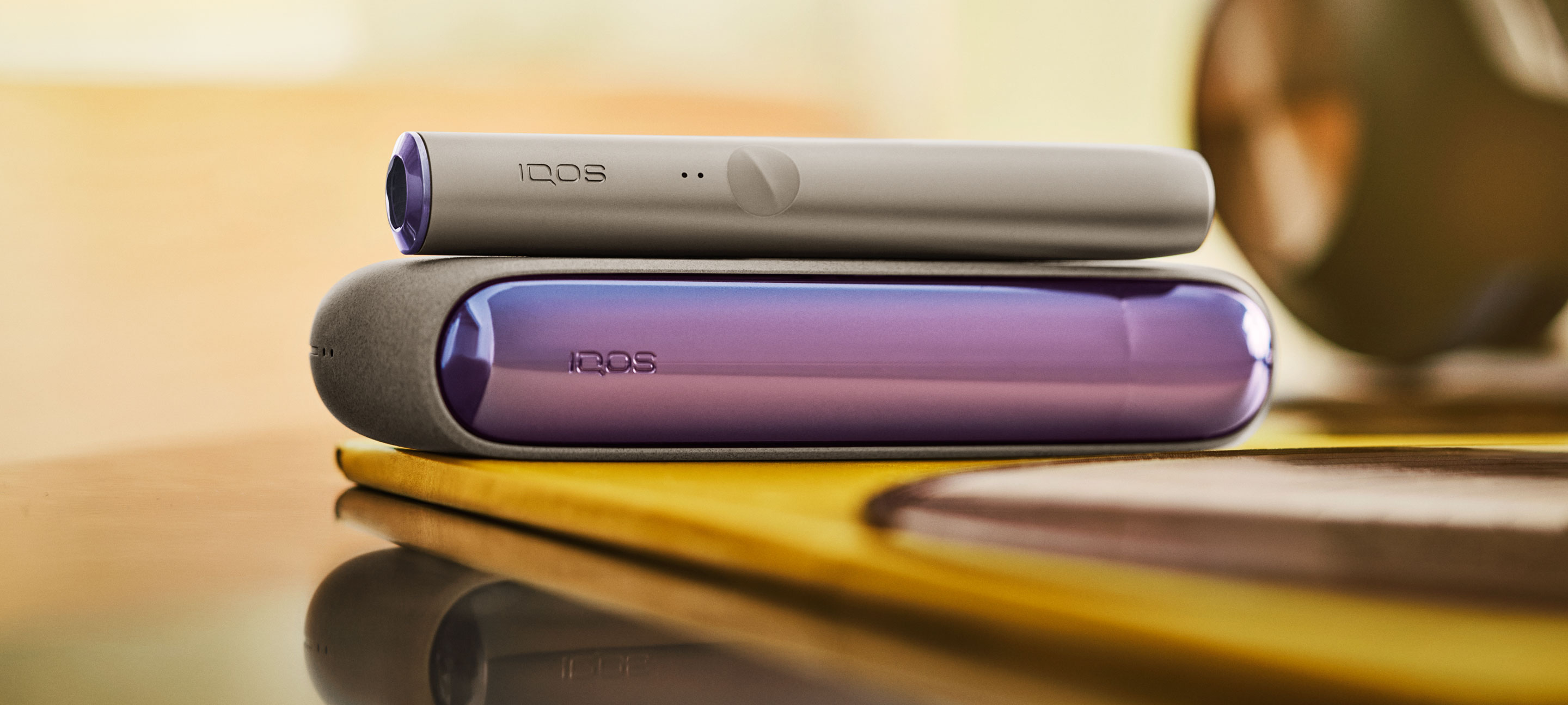 An IQOS ILUMA PRIME Holder and Pocket Charger on a table.