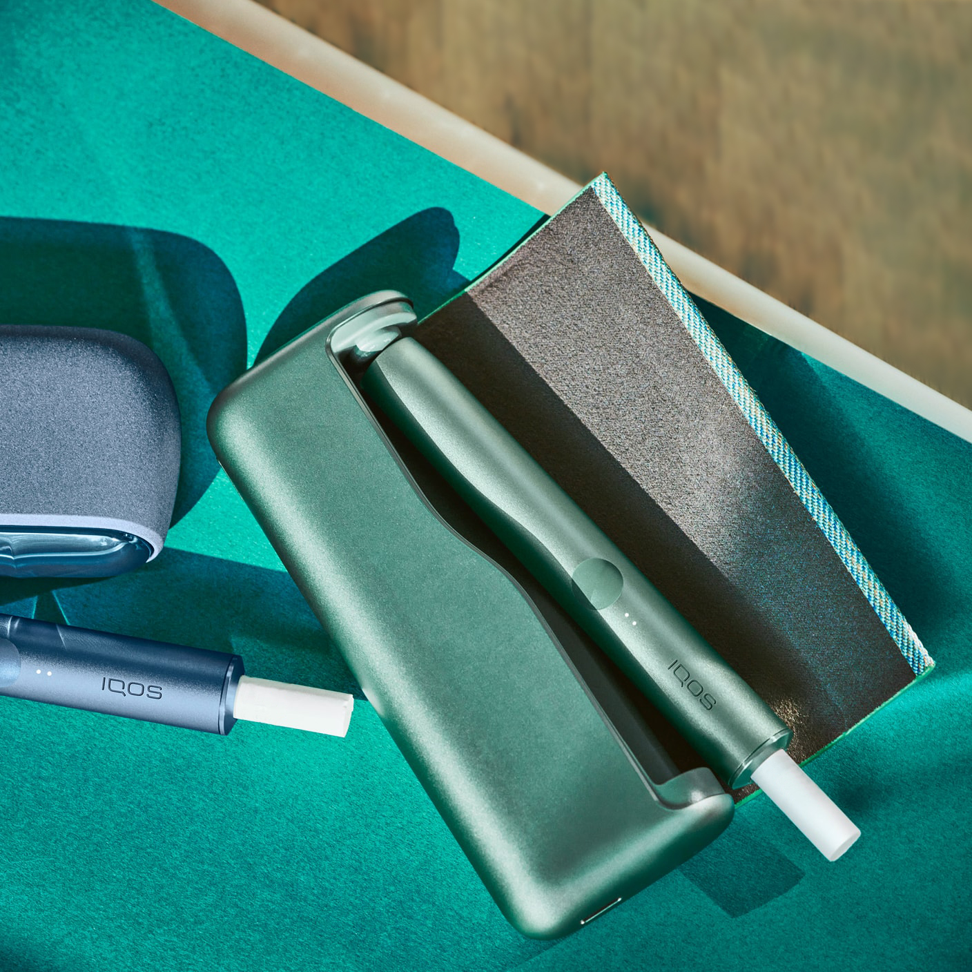 Jade green IQOS ILUMA device and charger on a desk.