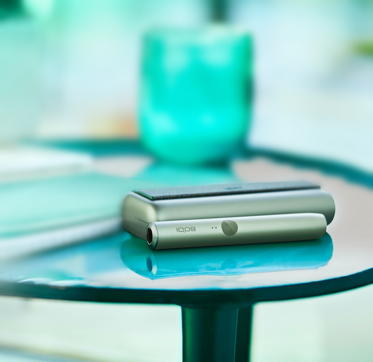 A jade green IQOS ILUMA device sits on a table.