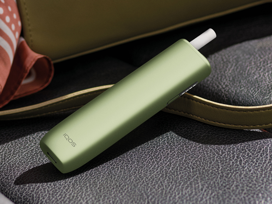 A Leaf Green IQOS ILUMA i ONE with a TEREA stick inserted, resting on the floor.