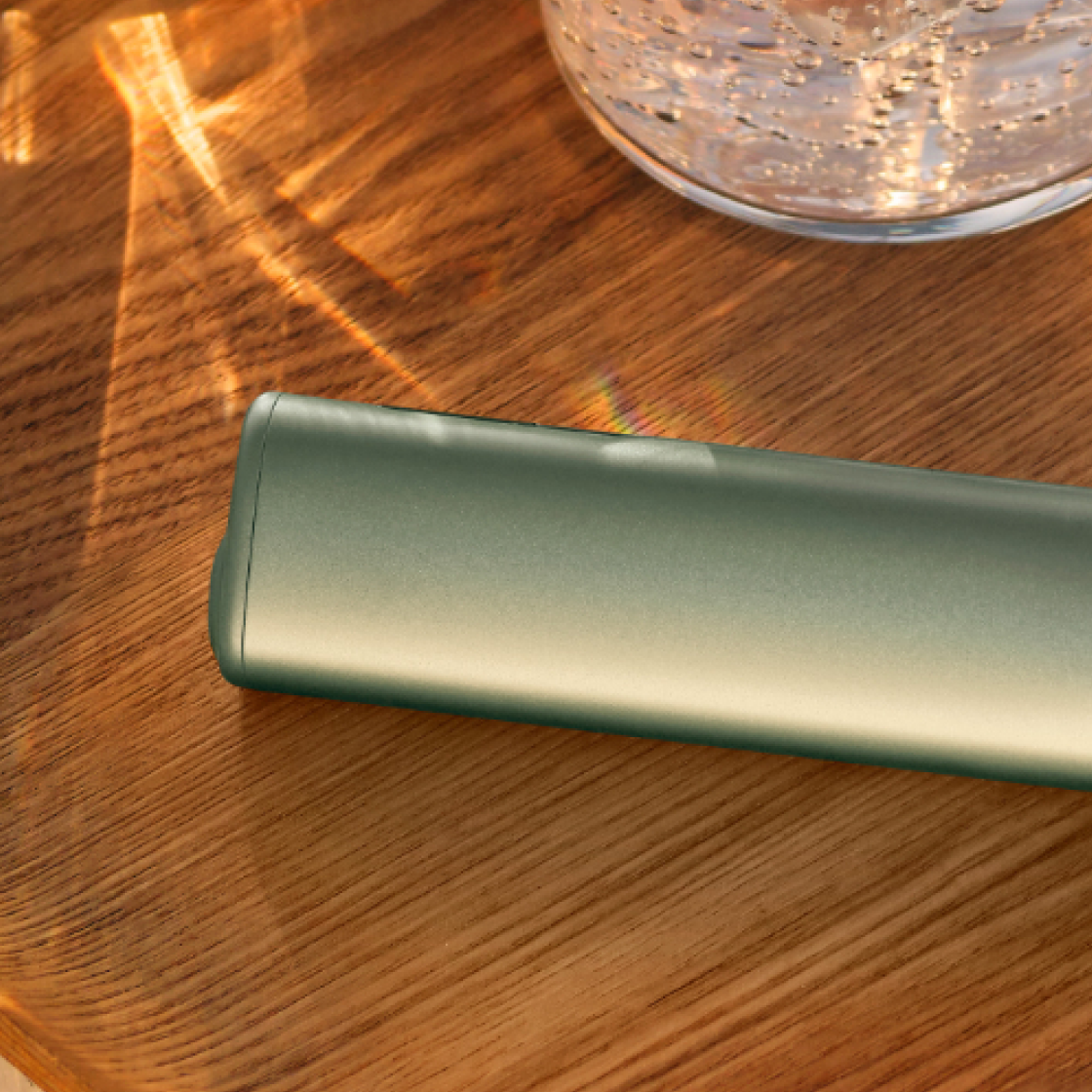 A Leaf Green IQOS ILUMA i ONE device on a wooden table.