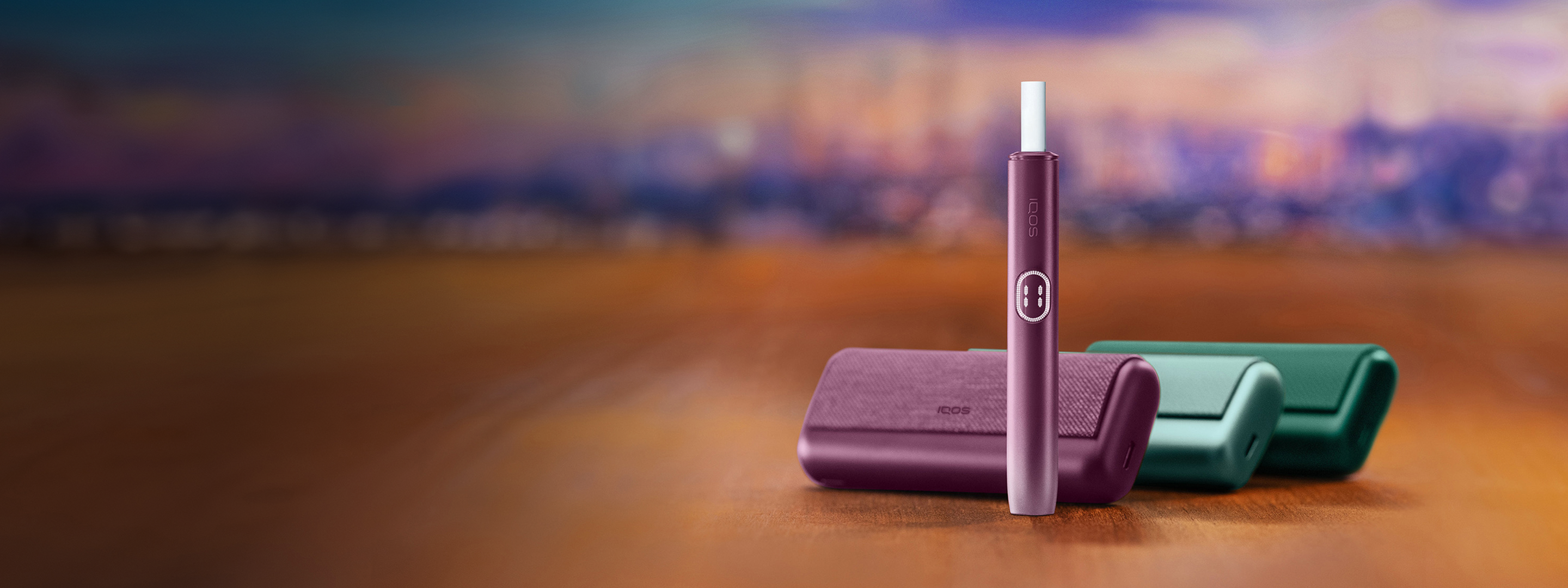 Breeze Blue and Aspen Green IQOS ILUMA i PRIME devices lying next to a Midnight Black IQOS ILUMA i PRIME device with a TEREA stick inserted.