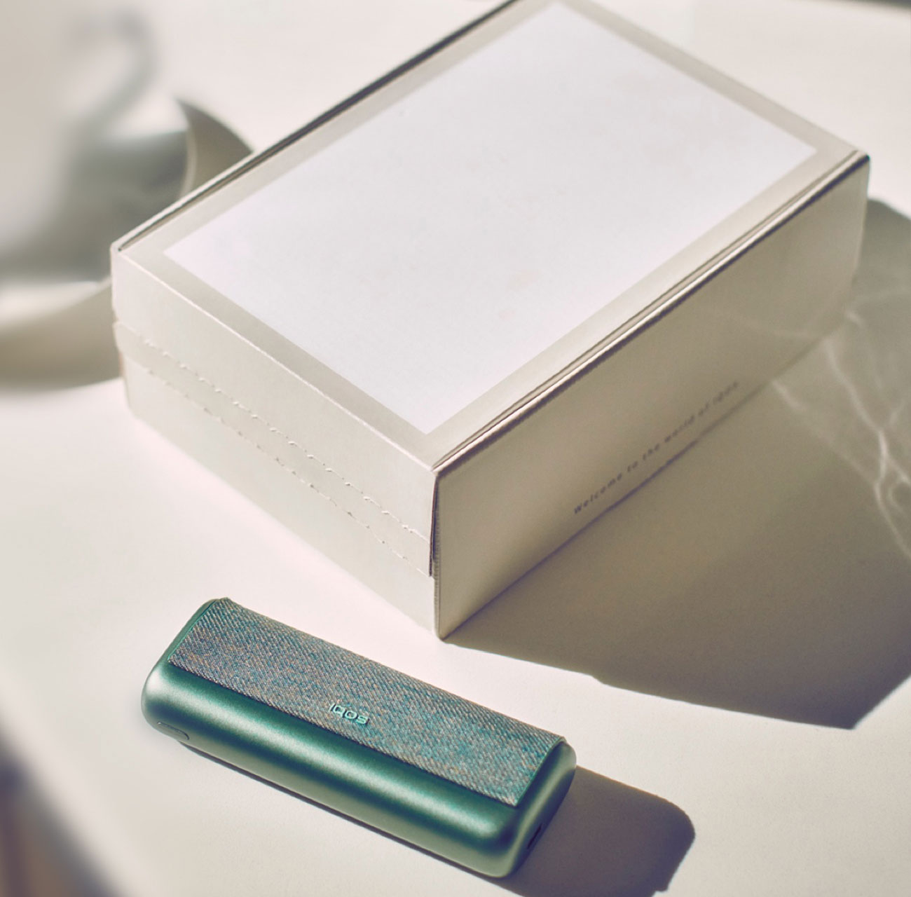 A jade green IQOS device on a table next to an IQOS product box.