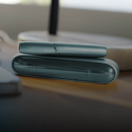 Turquoise IQOS Originals Duo holder and pocket charger on a wooden table.
