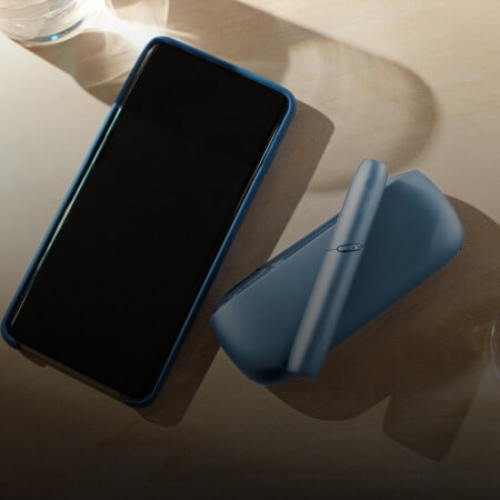 IQOS Originals Duo Holder and Pocket Charger in turquoise color on a table.